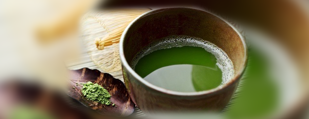 Bowl of green matcha beside a bamboo whisk and matcha powder